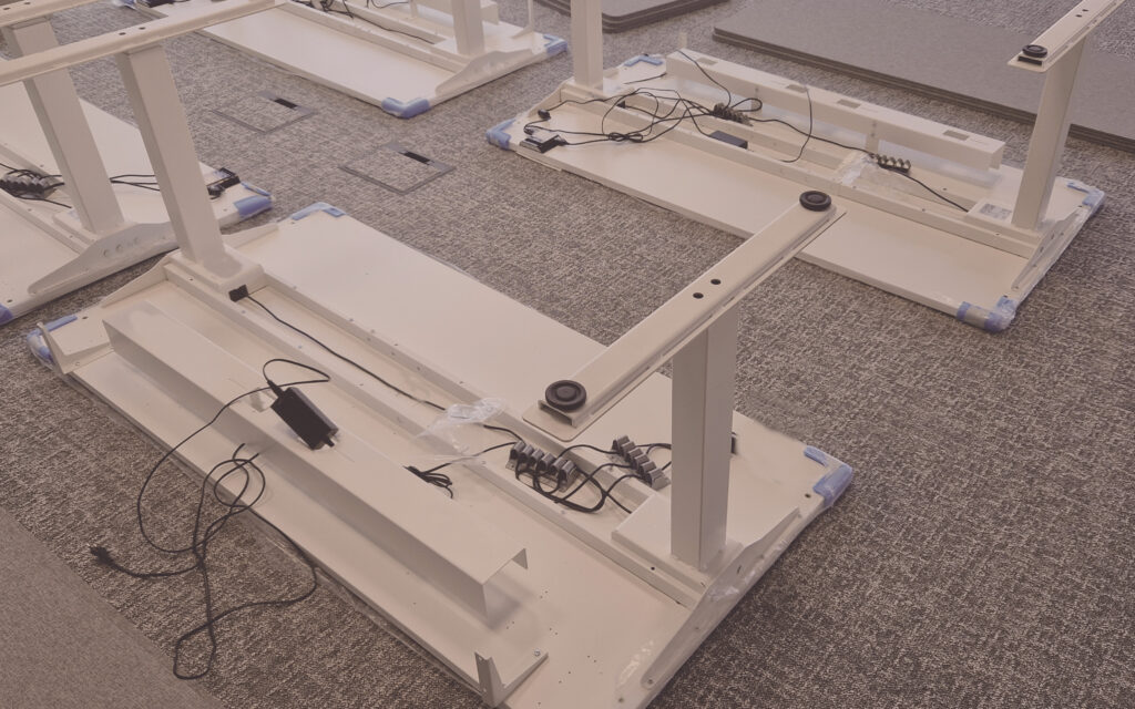 Praxisübung in der Schulung für technische Montage: Höhenverstellbare Schreibtische werden fachgerecht montiert und verkabelt.